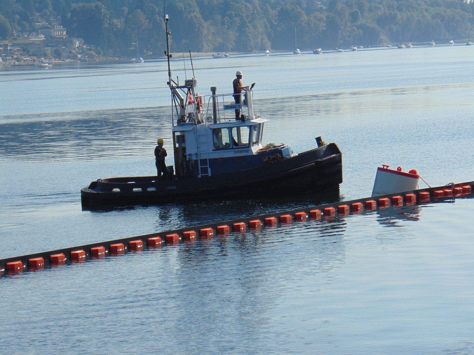 Tug Demac II deploying oil containment boom across harbour