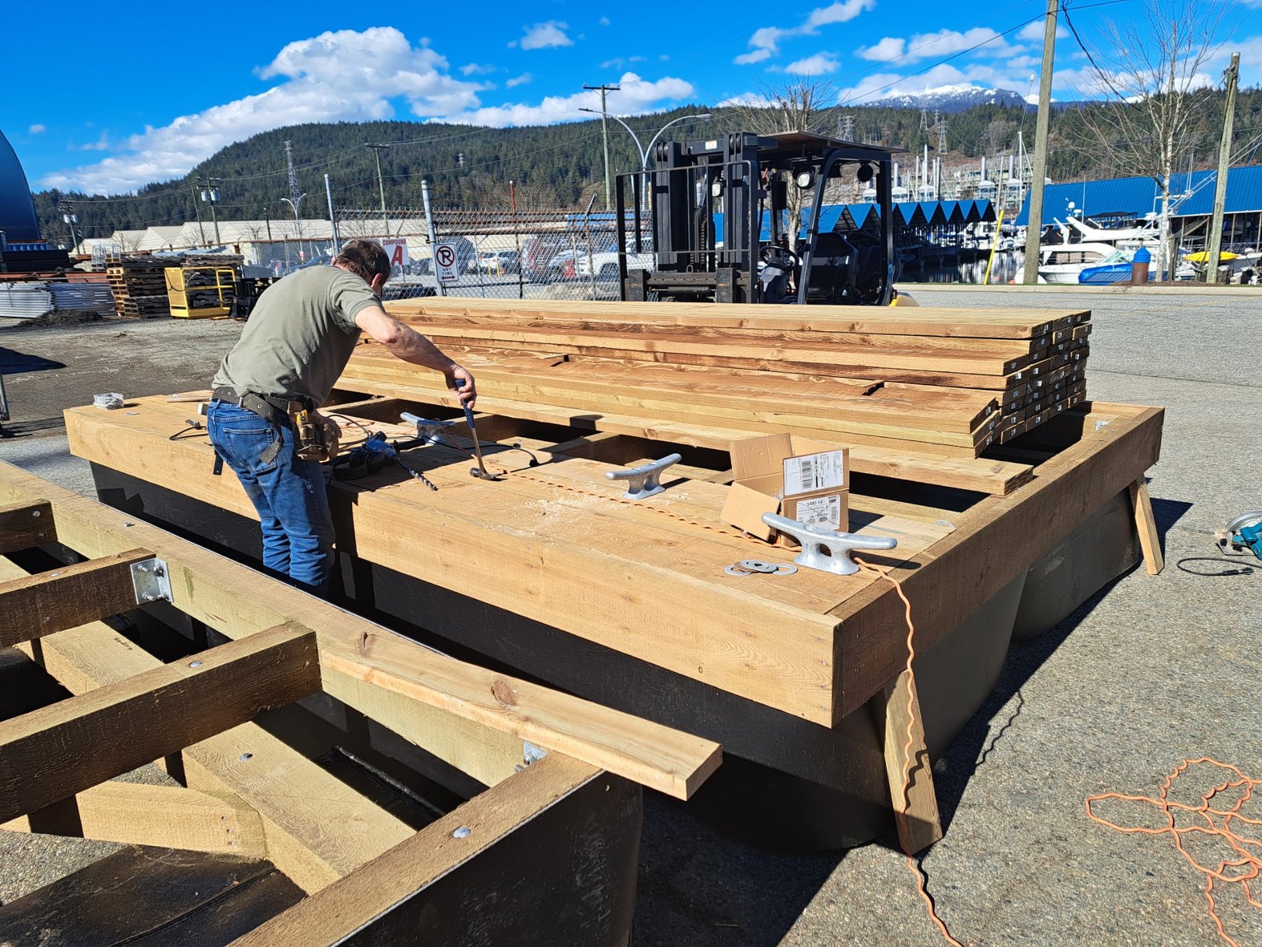 Installing cleats and decking on floating dock at marina work yard